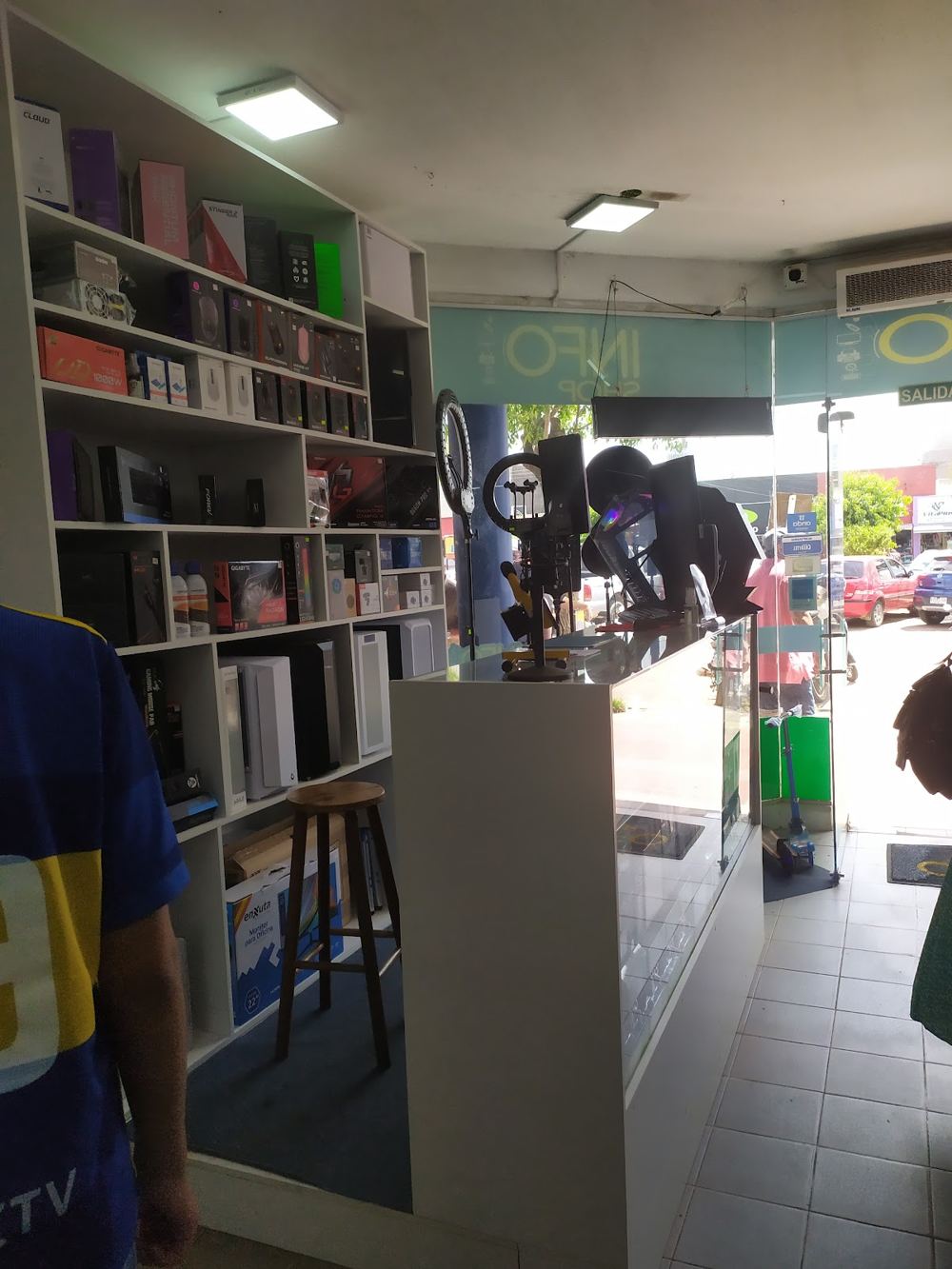 Interior de Info Shop con estantes de componentes y accesorios de computación, y el cartel del local al fondo
